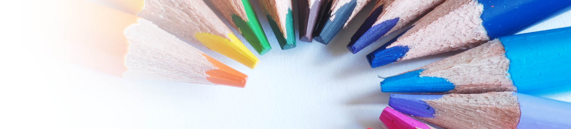 Farbige Buntstifte sind in einem Halbkreis mit der Mine zueinander und farblich von lila bis orange sortiert und angeordnet. Vermittelt wird ein Zusammenkommen von Vielfalt und Individualität.